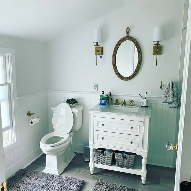 Finished bathroom with white beadboard wainscot, soft grey-green walls, a rope mirror and brass sconces